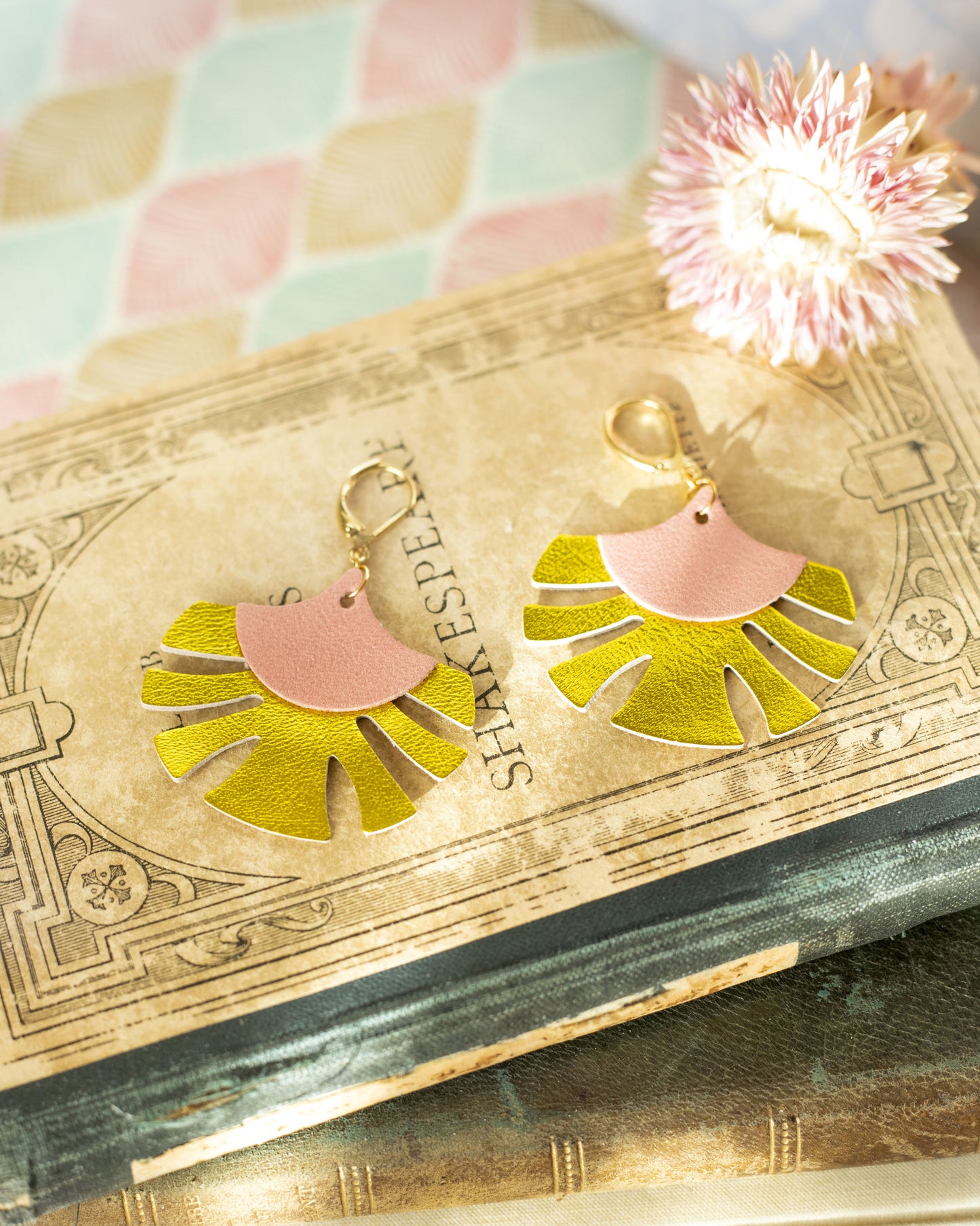 Boucles d'oreilles cuir rose et chartreuse en forme de palmes posées sur un livre ancien avec une fleur