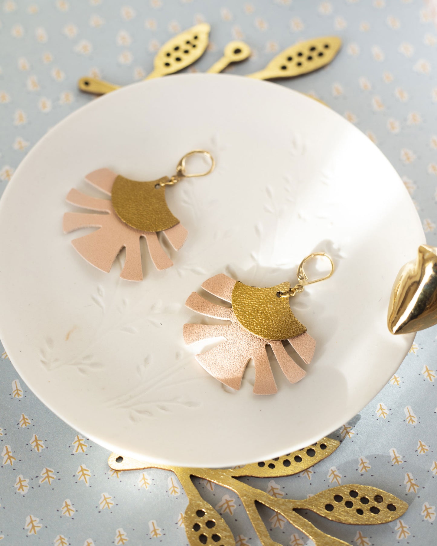 Boucles d'oreilles cuir bronze rose de Chenoha Studio posées sur une assiette blanche décorative