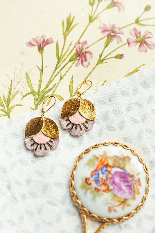 Boucles d'oreilles fleurs de cerisier doré et rose élégantes posées sur un tissu avec une loupe vintage