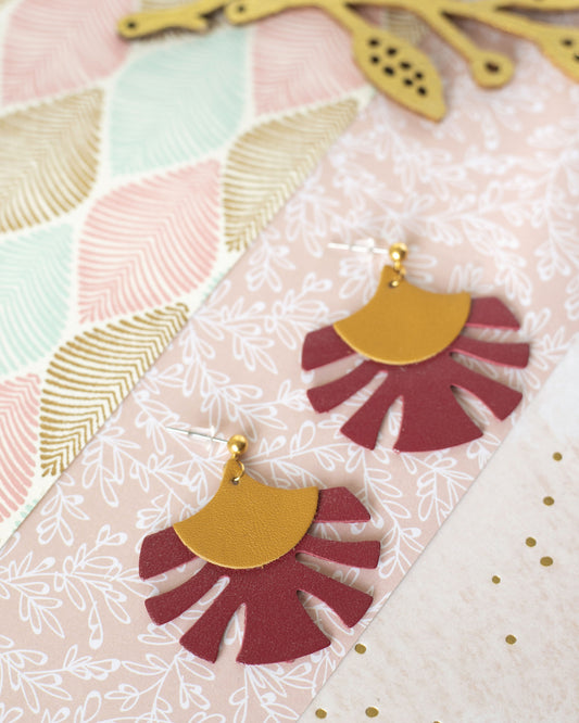 Boucles d'oreilles Palmes cuir ocre jaune et rouge bordeaux signées Chenoha Studio posées sur fond décoratif
