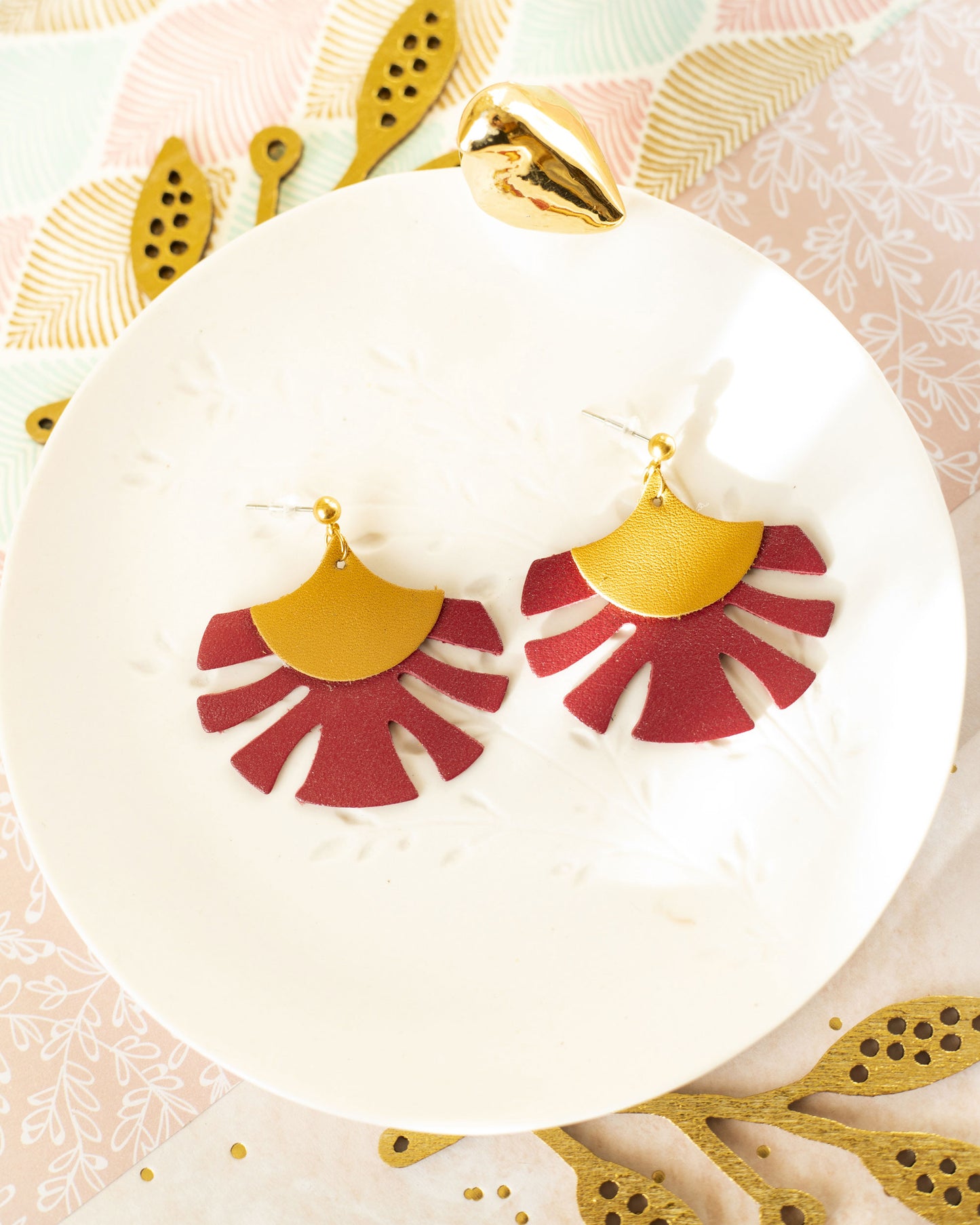 Boucles d'oreilles Palmes cuir ocre jaune et rouge bordeaux posées sur une assiette blanche