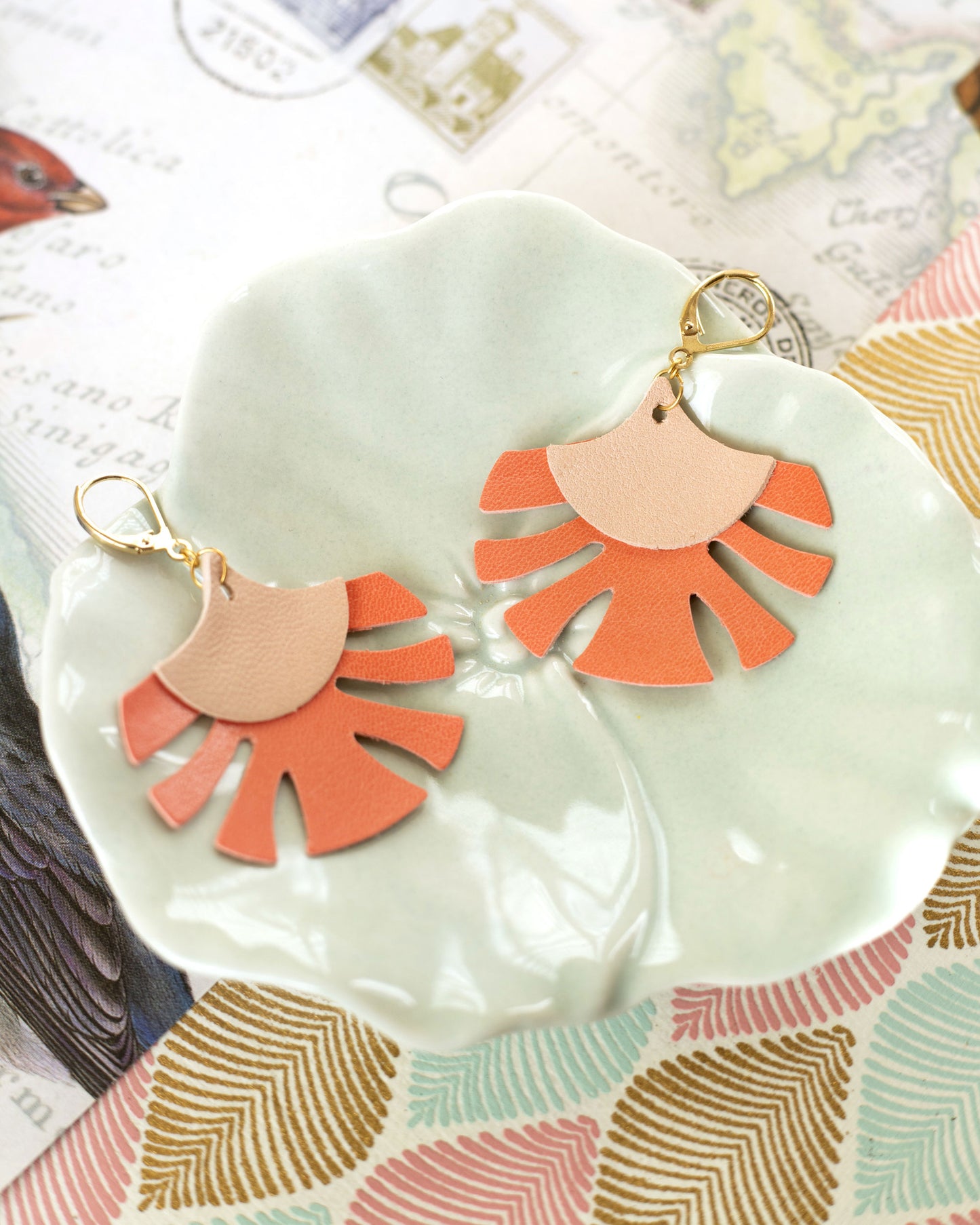 Boucles d'oreilles Palmes cuir rose chair et capucine de Chenoha Studio posées sur un plat vert clair