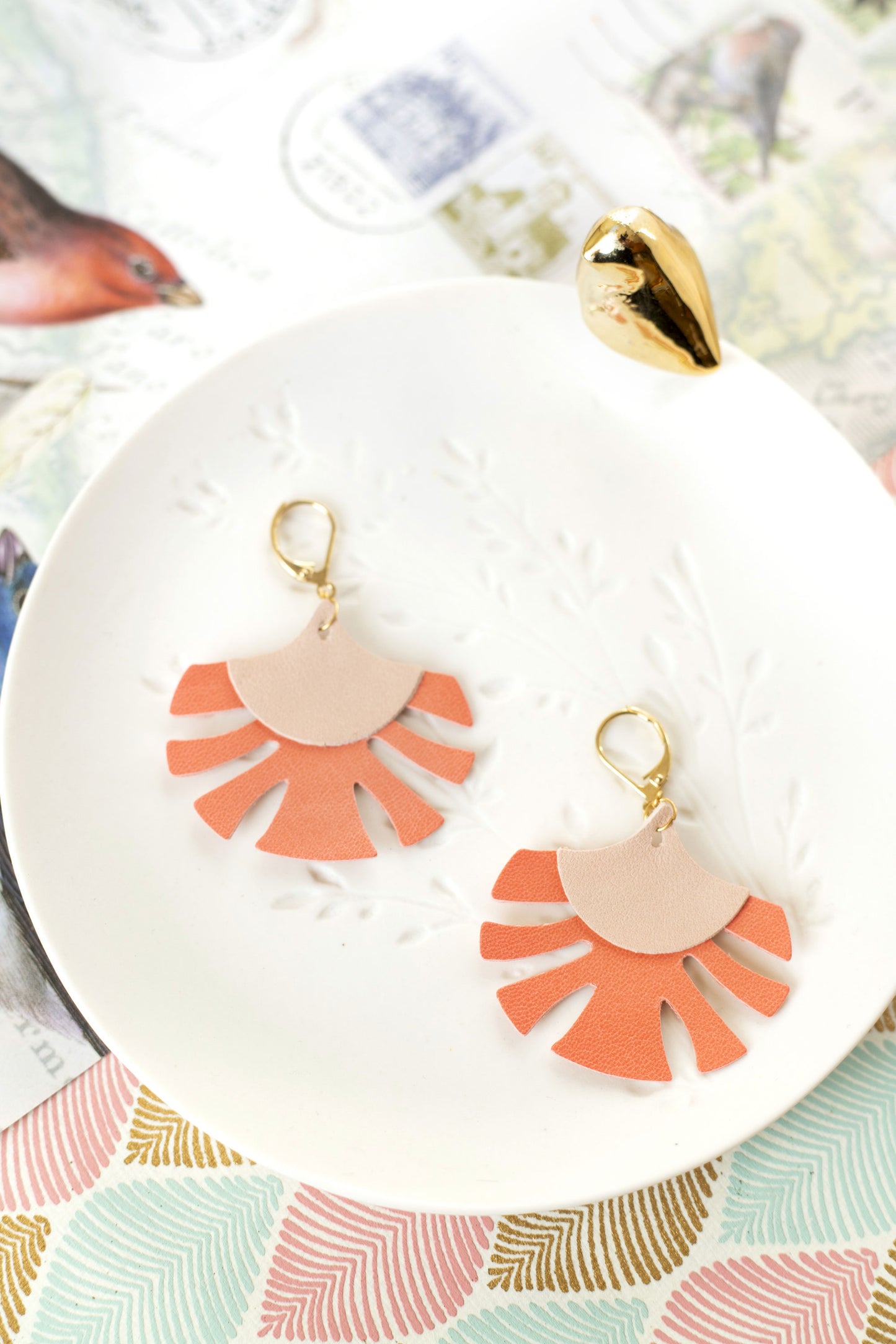 Boucles d'oreilles Palmes cuir rose chair et capucine posées sur une assiette blanche décorative