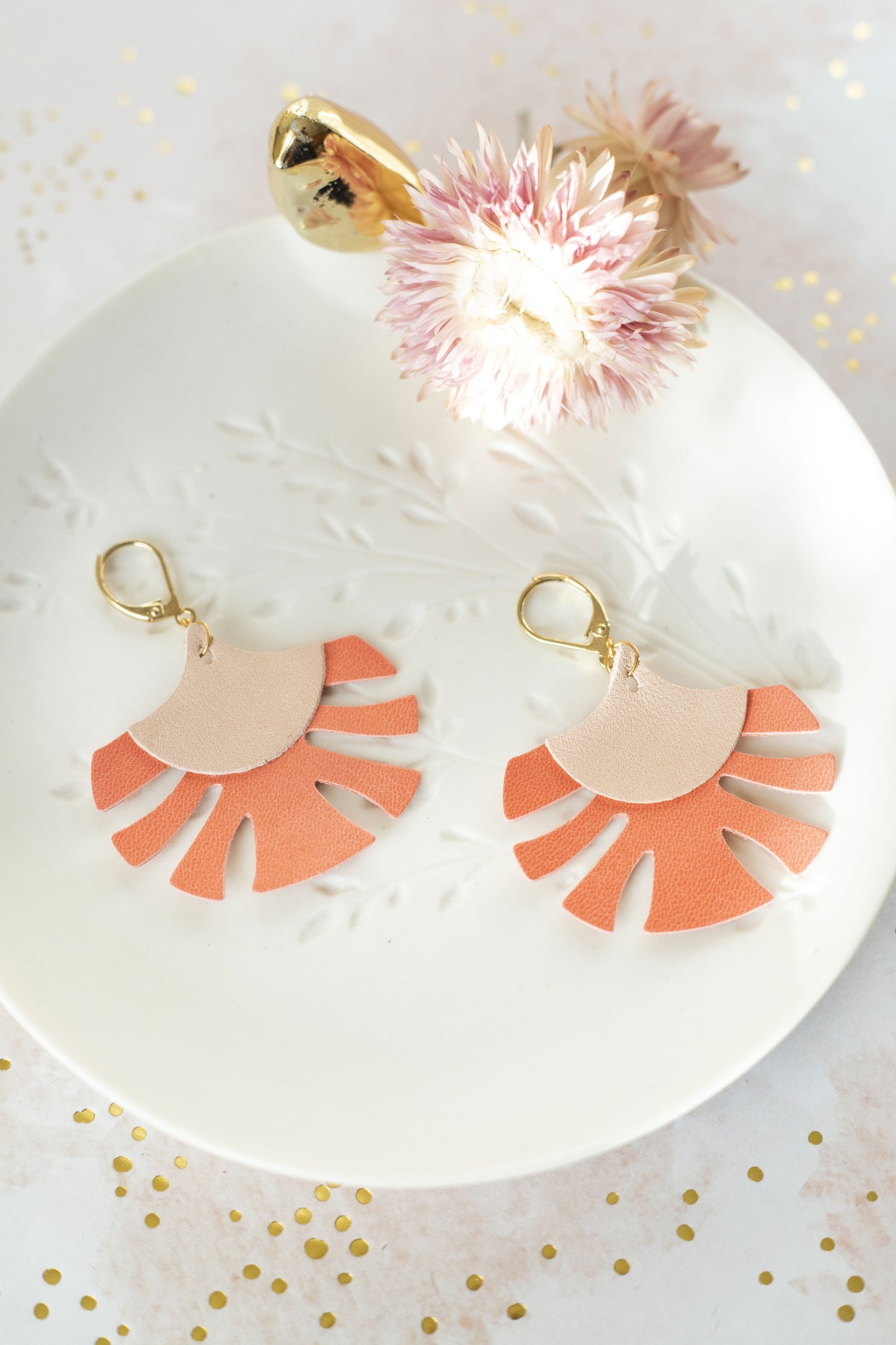 Boucles d'oreilles Palmes cuir rose chair et capucine de Chenoha Studio posées sur une assiette blanche décorée