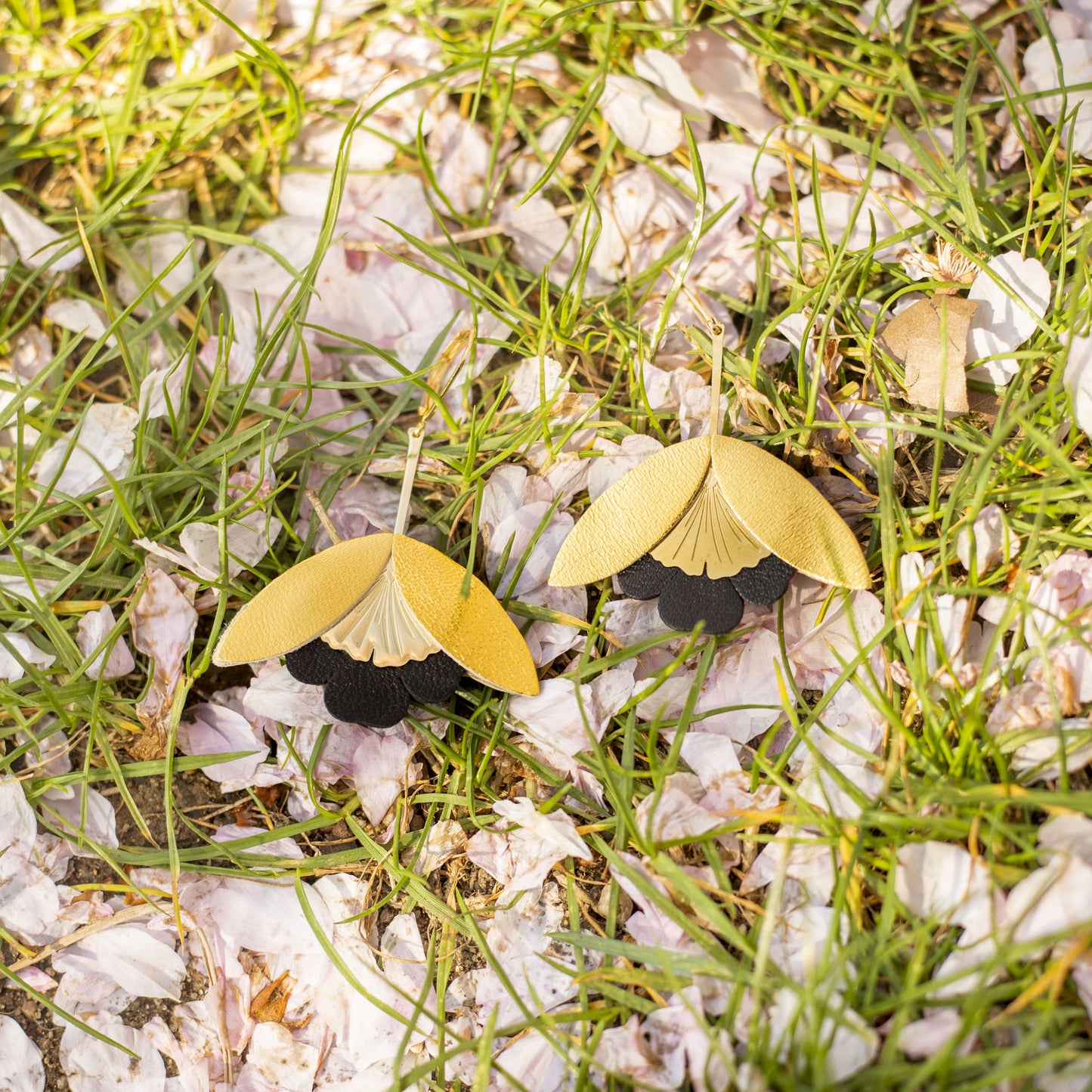 Boucles d'oreilles Fleurs de Ginkgo cuir doré et noir posées sur herbe et pétales blancs