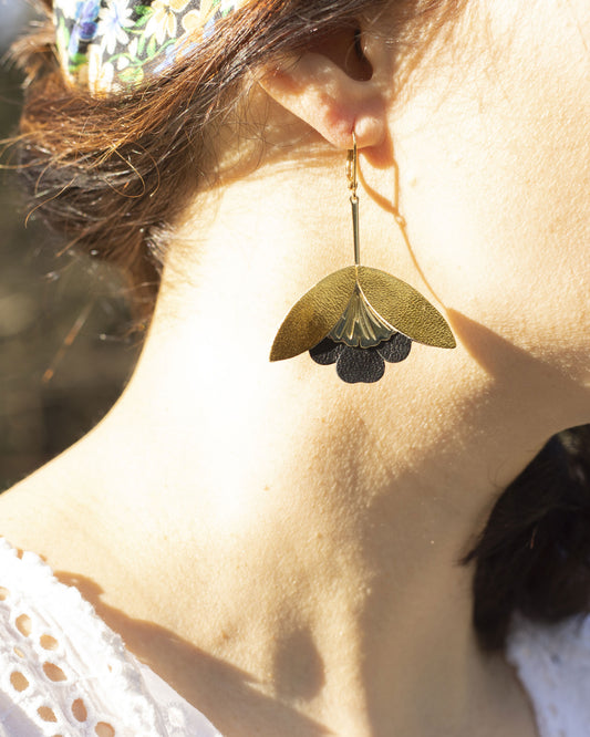 Boucles d'oreilles Fleurs de Ginkgo cuir doré et noir portées par une femme en lumière naturelle