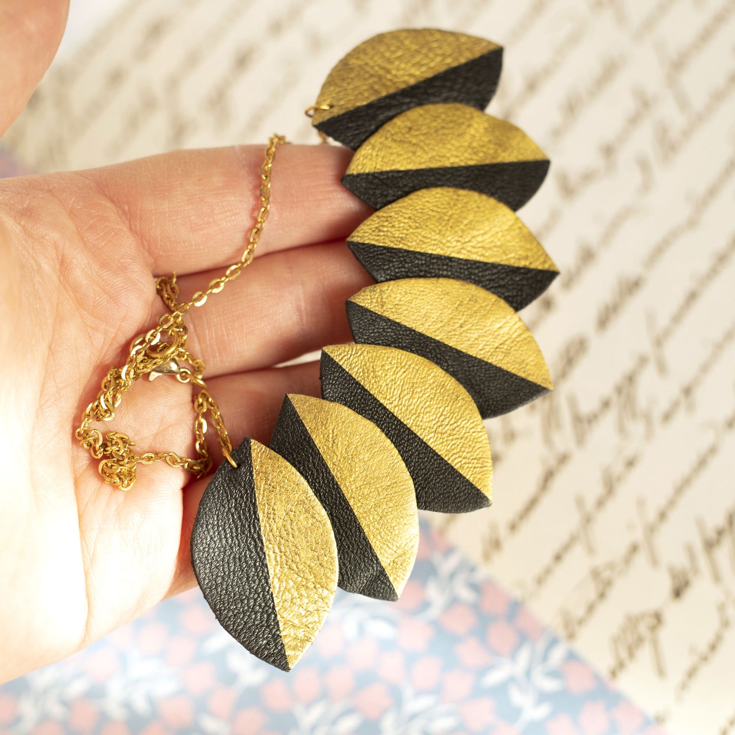 Collier plastron cuir recyclé noir et doré feuilles ovales tenu dans une main
