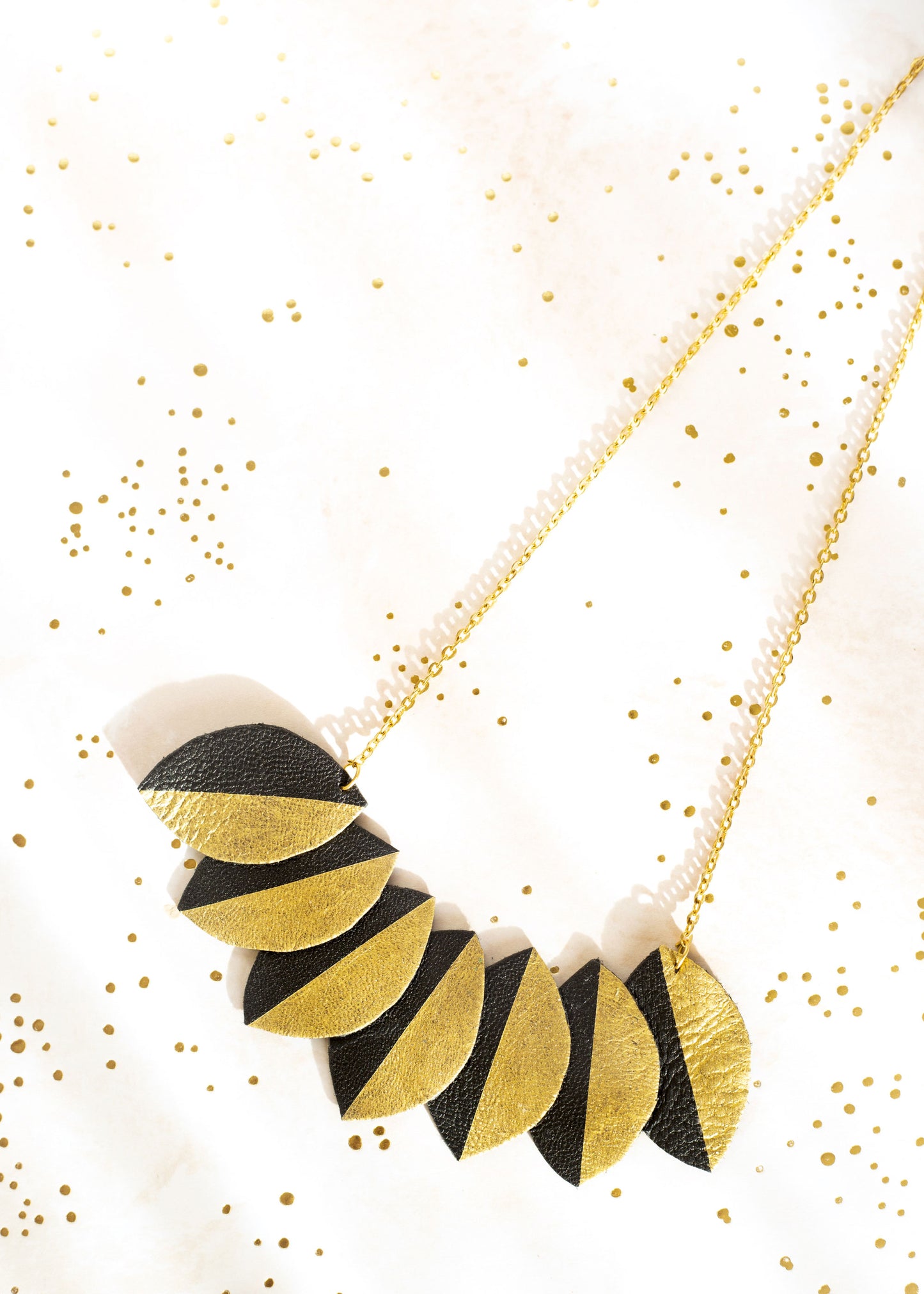 Collier plastron cuir recyclé Chenoha Studio en feuilles noires et dorées sur chaîne fine dorée