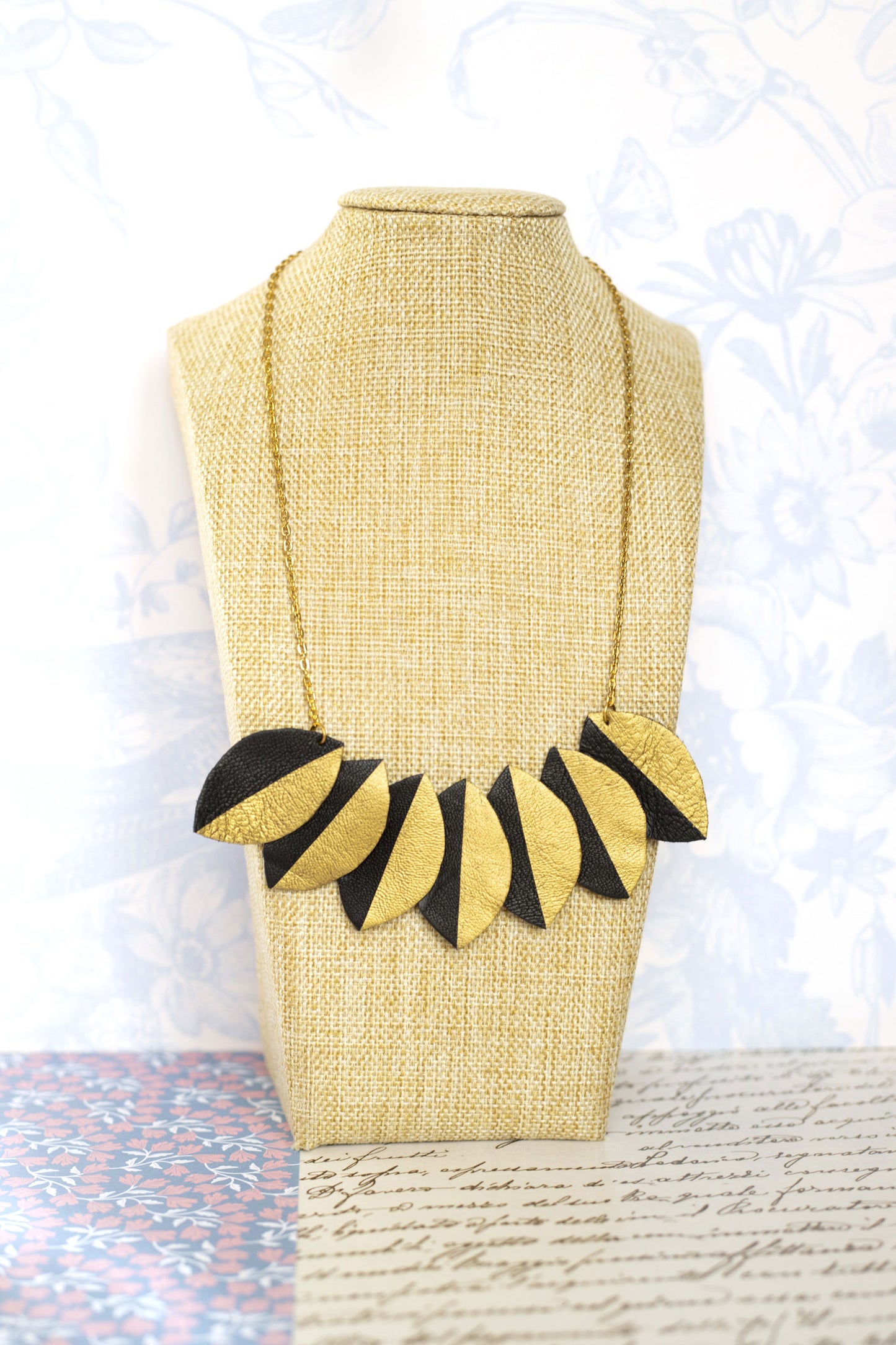 Collier plastron cuir recyclé noir et doré avec formes géométriques présenté sur un support beige