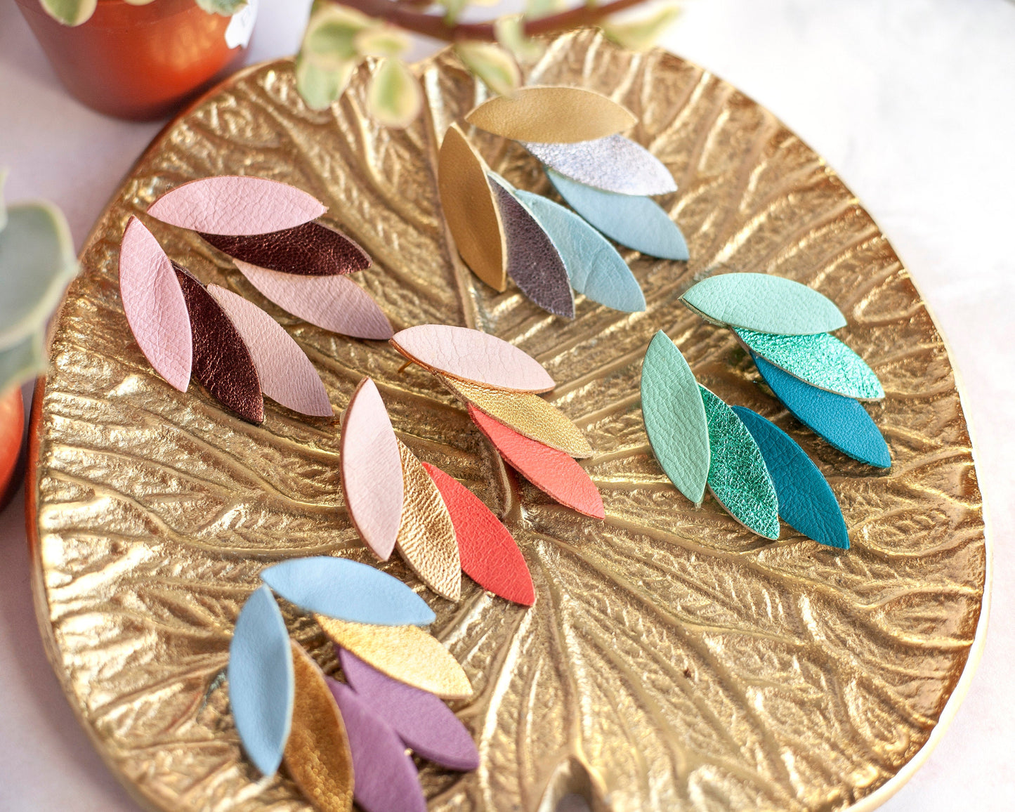 Boucles d'oreilles cuir vert bleu et autres couleurs présentées sur un plateau doré en forme de feuille