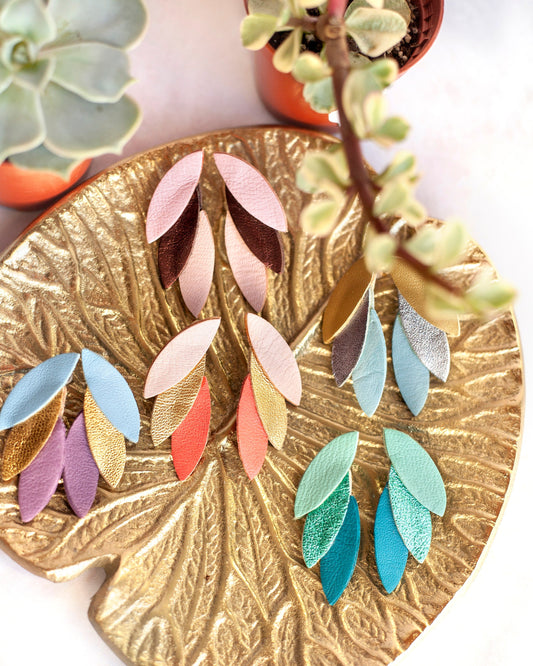 Boucles d'oreilles cuir vert bleu et autres couleurs disposées sur un plateau doré feuille par Chenoha Studio
