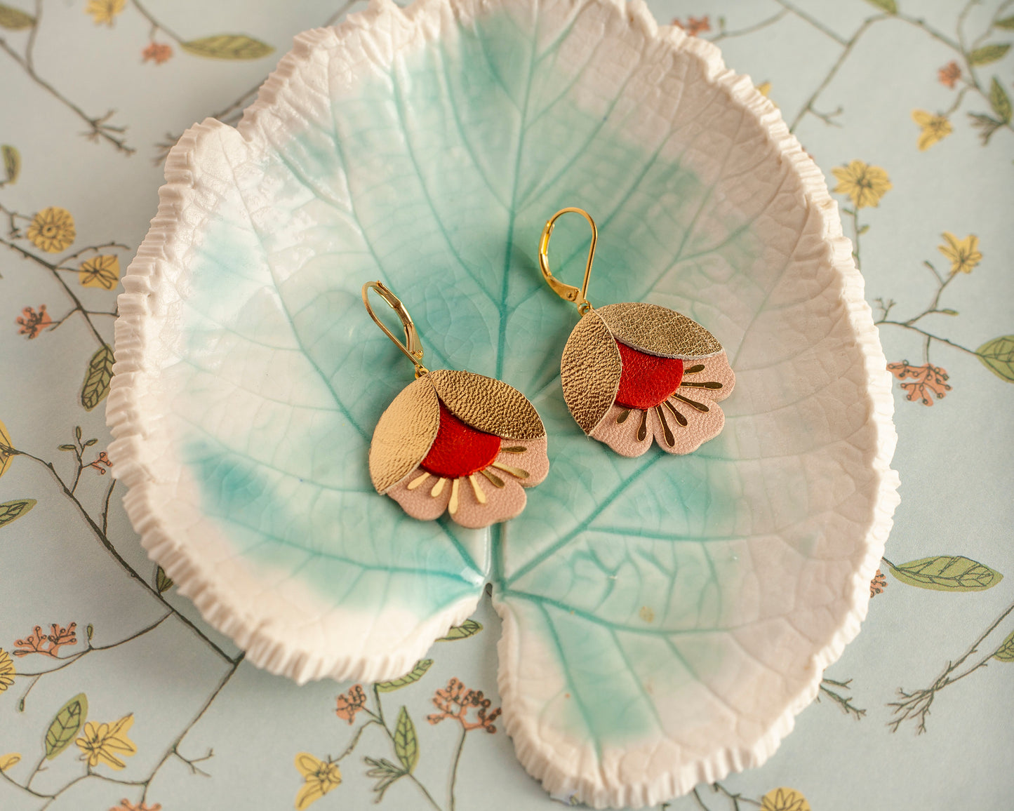Boucles d'oreilles fleurs de cerisier cuir doré rouge et rose posées dans un plat en forme de feuille