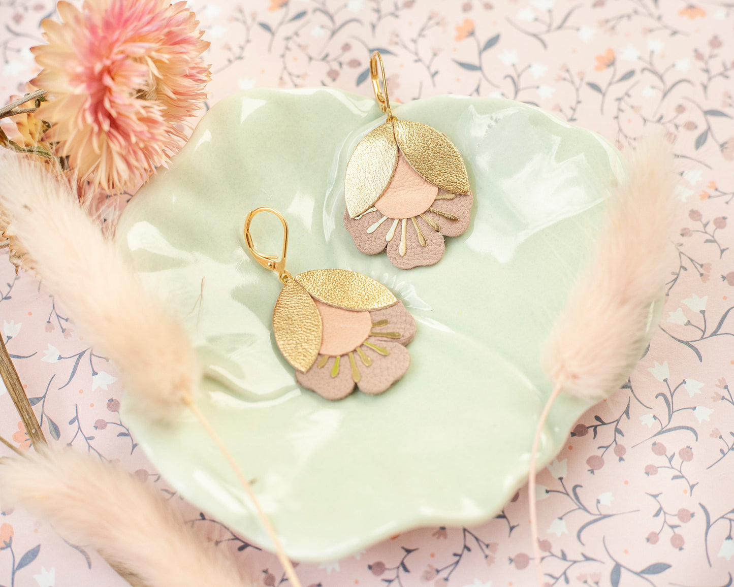 Boucles d'oreilles fleurs de cerisier doré et rose posées sur une assiette verte pastel décorative
