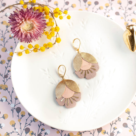 Boucles d'oreilles fleurs de cerisier doré et rose posées sur une assiette blanche avec fleurs séchées