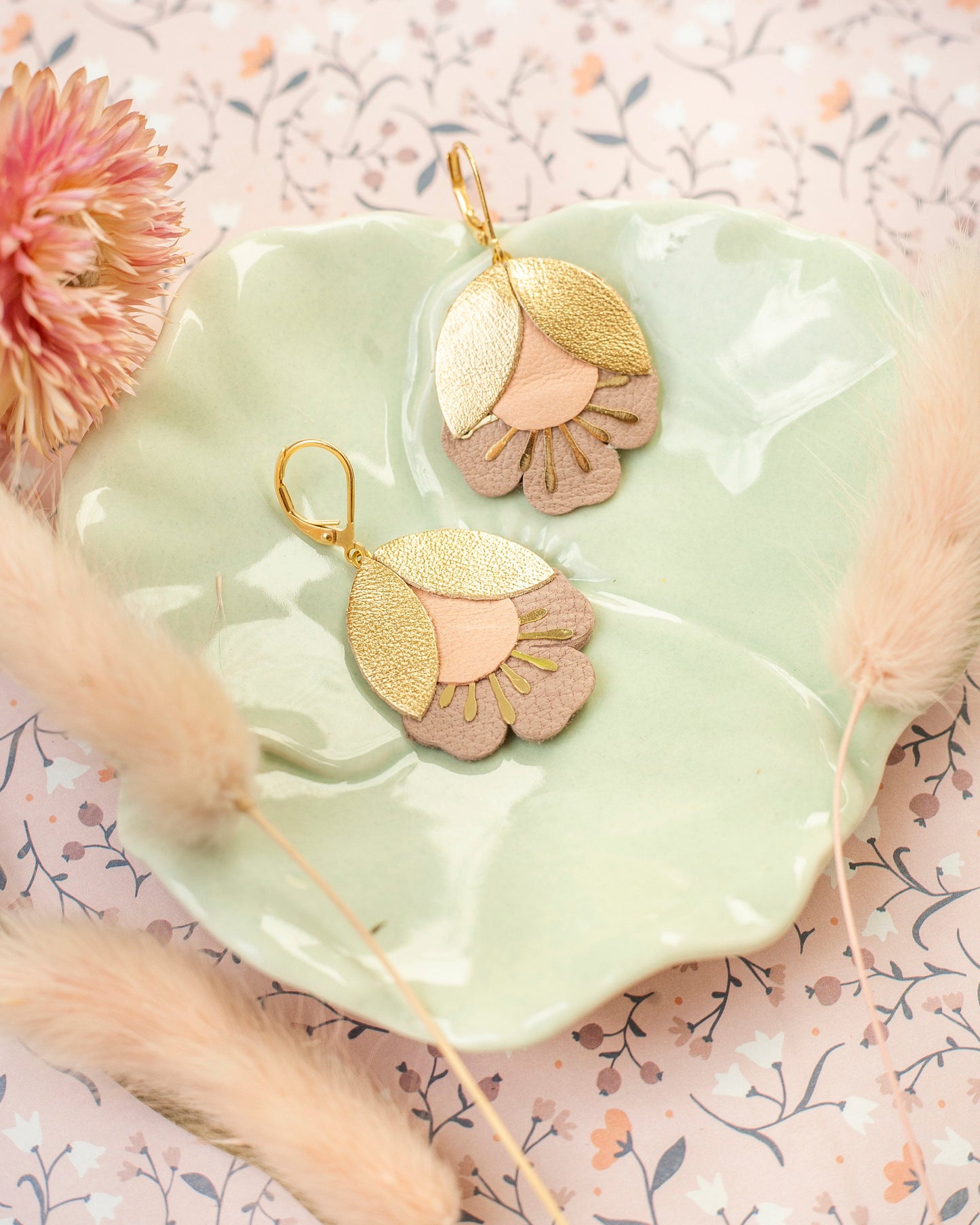Boucles d'oreilles fleurs de cerisier doré et rose posées sur assiette verte pastel avec décor floral