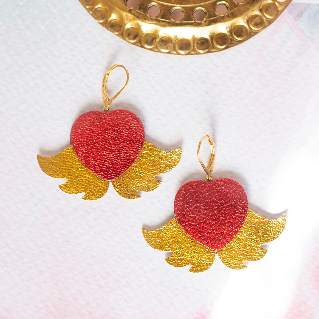 Ohrringe mit geflügelten Herzen aus Gold und metallisch rotem Leder