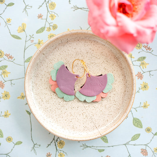 Boucles d'oreilles eventails cuir turquoise mauve doré posées dans une assiette beige